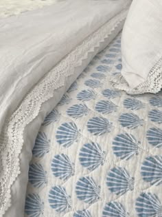 a white and blue bedspread on a bed next to a pillow with lace