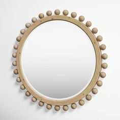 a round mirror with wooden beads hanging on it's sides and a white wall in the background