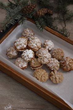 a tray filled with cookies and powdered sugar on top of a wooden table next to pine branches