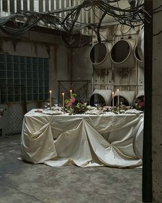 the table is covered with white cloth and has candles on it in front of an old building