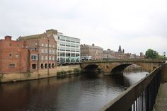 a bridge over a river with buildings on both sides and a train crossing the bridge