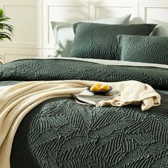 a bed with green bedspread and pillows on top of it next to a potted plant