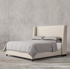 a bed sitting on top of a wooden floor next to a gray wall with a white headboard