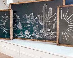 two black and white pictures on a shelf in a room with wooden frames, cactuses and mountains