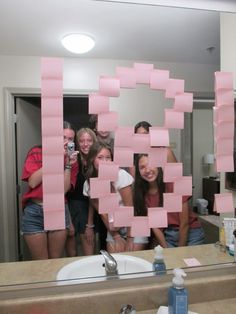 a group of people standing in front of a bathroom mirror with pink sticky notes on it