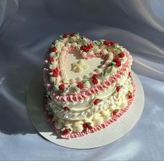 a heart shaped cake on a plate with white and pink frosting, topped with cherries