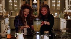 two women standing in a kitchen with a blender on the counter and one woman pointing at it