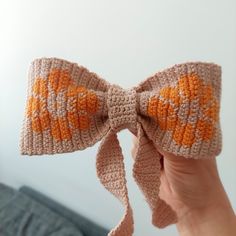 a hand holding up a crocheted bow with orange and white designs on it