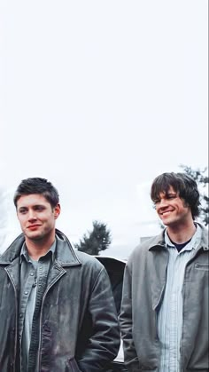 two young men standing next to each other in front of a building with trees behind them