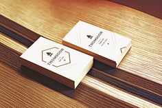 two white business cards sitting on top of a wooden table next to eachother