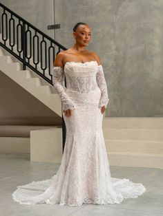 a woman standing in front of a staircase wearing a white wedding dress with long sleeves