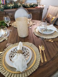 the table is set for christmas dinner with gold and white plates, silverware, and napkins