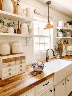 a white kitchen with wooden counter tops and open shelving on the wall above it