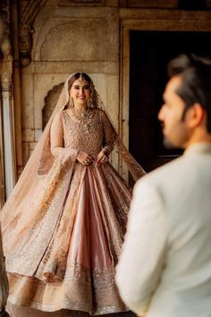 a man standing next to a woman in a pink dress and veil on her wedding day