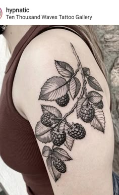 a woman's shoulder with black and white tattoos on her arm, showing the leaves and berries