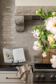 an open book sitting on top of a stove next to a vase filled with flowers