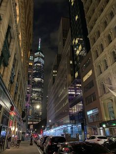 a city street at night with cars parked on the curb and tall buildings in the background