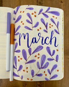 an open notebook with the word march written in blue and orange on it next to a pen