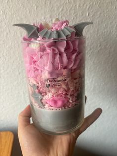 a person holding up a cup filled with pink and grey cake in it's hand