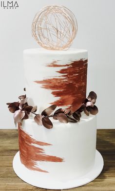 a white and brown cake on a wooden table with an artistic topper in the middle