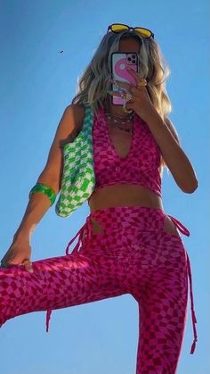 a woman wearing pink and green clothing holding a cell phone up to her face while standing in the air