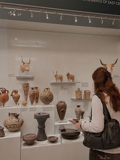 a woman looking at pottery on display in a museum