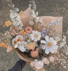 a person holding a bouquet of flowers in their hand on the ground with grass behind them