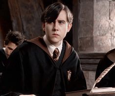 two young men sitting at a desk in front of a harry potter book and quill