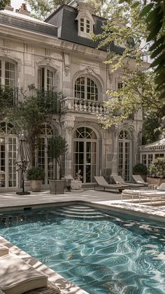 an outdoor swimming pool in front of a large house with lots of windows and doors