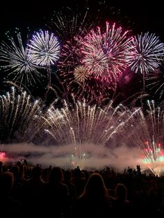 fireworks are lit up in the night sky with people standing around and watching from their seats