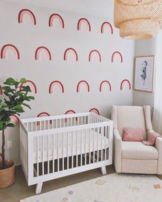 a baby's room with a crib, chair and potted plant