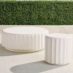 two white tables sitting next to each other in front of a hedge