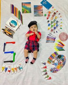 a baby laying on top of a white sheet covered in art supplies