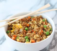 rice with peas and carrots in a white bowl next to wooden chopsticks