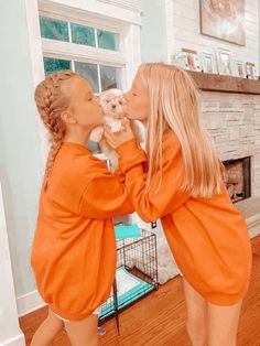 two women kissing each other in front of a fireplace with a dog on her lap