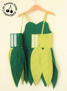 two green leaves are attached to a hanger on a white wall, one is made from paper and the other is made out of cardboard