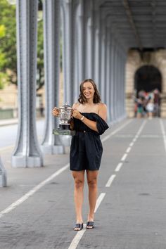 a woman is standing on the street holding a trophy and smiling at the camera with her hands in her pockets