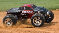 a red and black remote control truck driving on the dirt with grass in the background