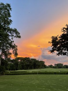 the sun is setting over a golf course with trees in the foreground and green grass on the far side