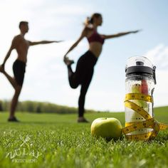 a man and woman standing in the grass with measuring tape around their waists next to an apple