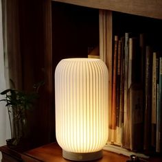 a white lamp sitting on top of a wooden table next to a bookshelf