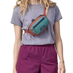 a woman wearing purple shorts and a gray t - shirt is holding a blue fanny bag