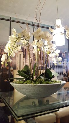 white flowers in a bowl on top of a glass table next to a cityscape