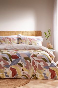 a bed with colorful comforter and pillows in a room next to a potted plant