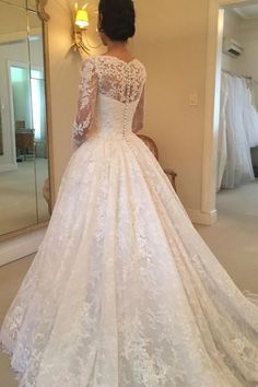 a woman in a white wedding dress looking at herself in the mirror with her back to the camera