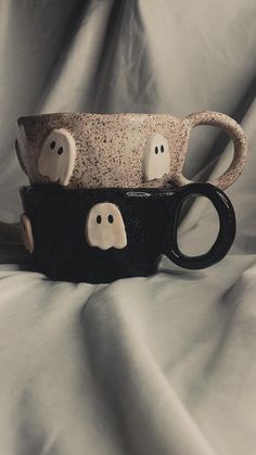 two coffee mugs decorated with ghost faces on a white cloth covered tablecloth in black and white