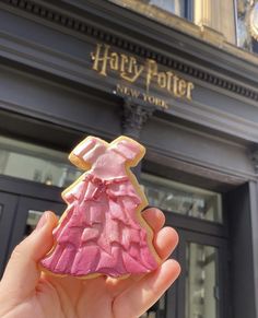 a hand holding up a pink dress shaped cookie in front of a harry potter building