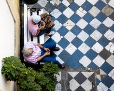 two people sitting on a bench next to a potted plant in front of a building