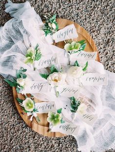 white flowers and greenery are arranged on a wooden platter with ribbons that say happily