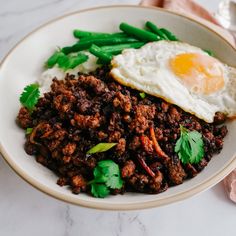 a white bowl filled with meat and eggs on top of a table next to napkins